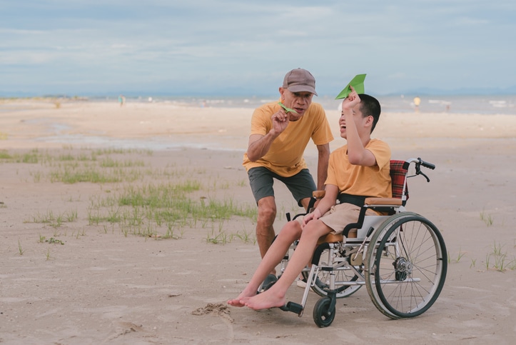 Dad and son in wheelchair experience paper plane activity on the beach with MediStays STA Australia