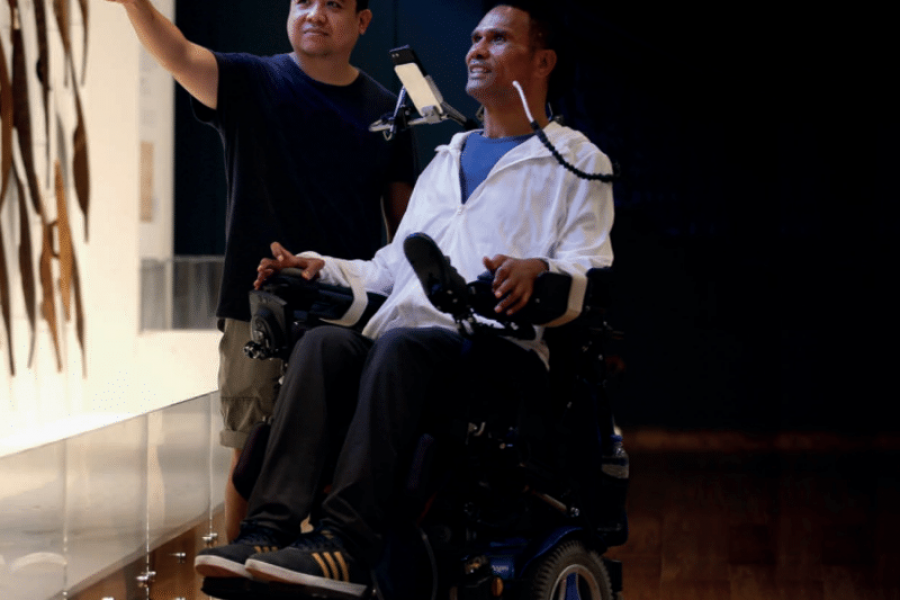 Man using a wheelchair in a museum looking at a feature with another man